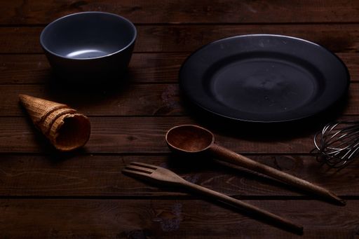 A closeup shot of wooden kitchen tools, a plate, bowl, cones on the table