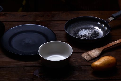 A closeup shot of a wooden kitchen tool, a potato, a plate, bowl, and a pan on the table