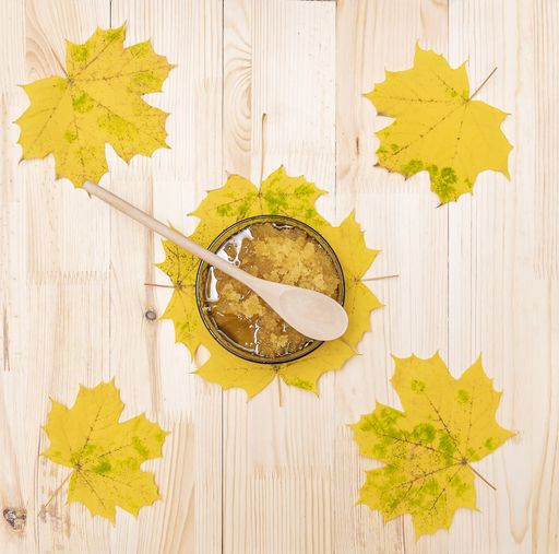 A cup with Bashkir honey and a wooden spoon stands on a wooden table surrounded by yellow leaves