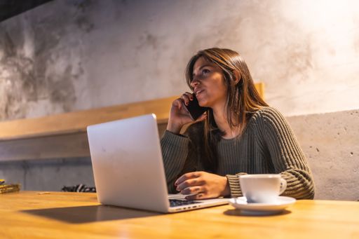 A young Caucasian female talking to a phone while working on a laptop at cafe