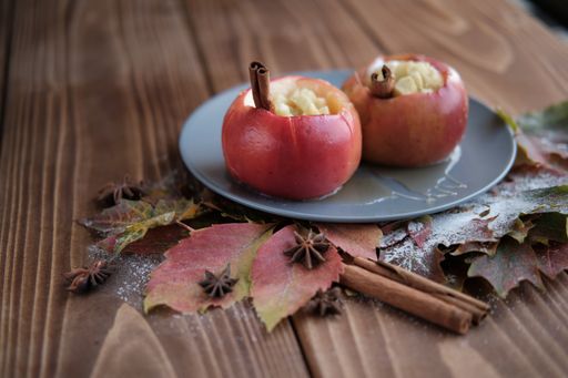 A closeup shot of baked apples with cinnamon and maple leaves on wooden table