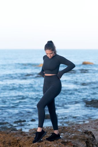 A young Latin female wearing black workout clothes, standing at the beach and posing