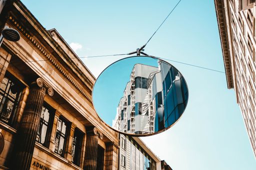 A beautiful modern building visible in a round mirror among old stone buildings