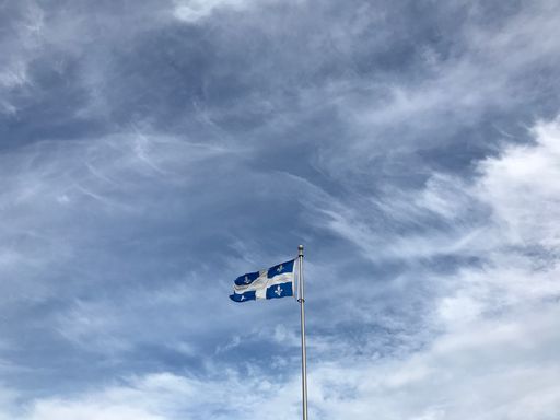 A low angle shot of the Quebec flag under the beautiful clouds in the sky