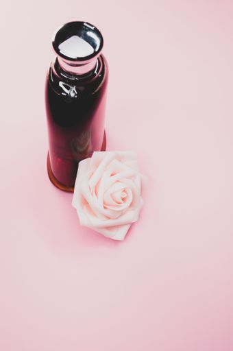 A bottle of nice perfume with a beautiful rose flower on a pink background