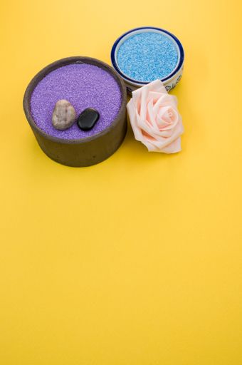 A closeup shot of aromatic bath pearls, beads and a rose flower on a yellow background with a copy space