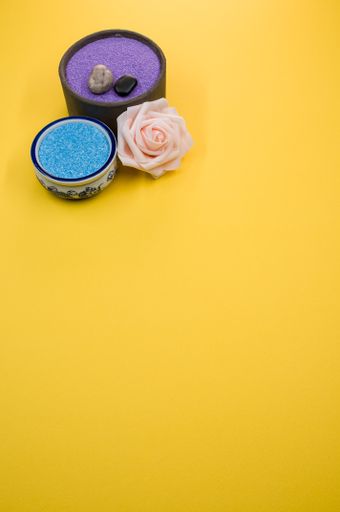 A closeup shot of aromatic bath pearls, beads and a rose flower on a yellow background with a copy space