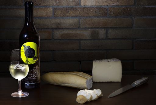A closeup of a white wine near a cheese with a baguette