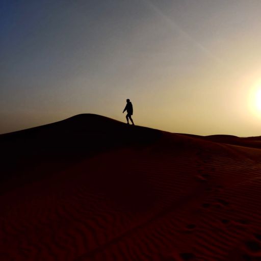 a silhouette of a man walking on desert sand under the sunshine