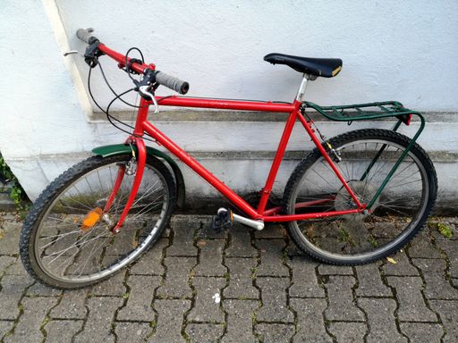 A red colored bicycle leaned on a white wall of a building with old brick flooring