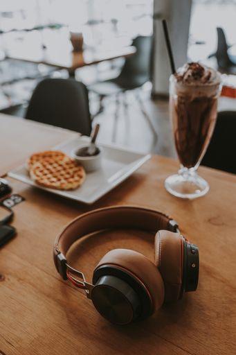 A vertical selective focus shot of headphones on a cafe table next to dessert