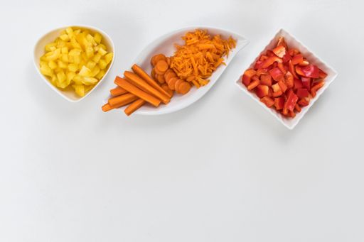 A top view of carrots, yellow peppers, and red peppers in white saucers isolated on white background