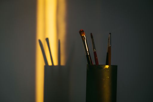 A closeup shot of painting brushes on the table with its shadow on the wall