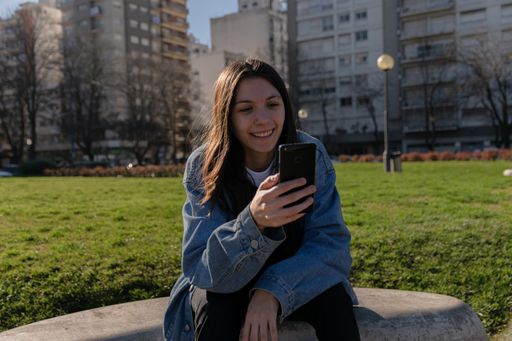 A closeup shot of a young lady with face piercings sitting outside smiling at her phone