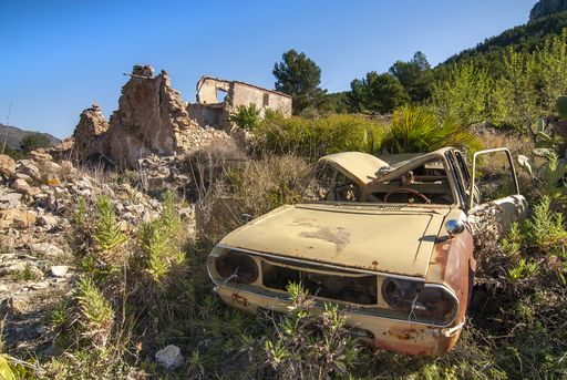 A closeup of an old abandoned car in a valley surrounded by building ruins and greenery