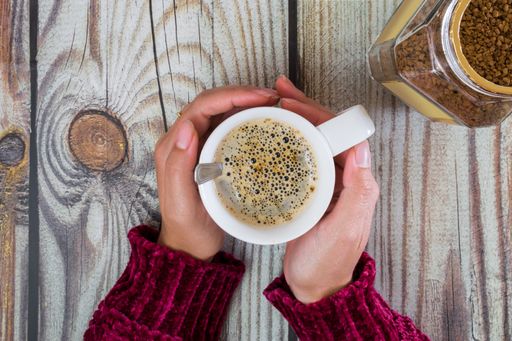 A top view of woman hands with a coffee cup on a wooden table