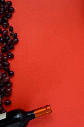 A top view of fresh ripe juicy grapes and a bottle of wine on a red background