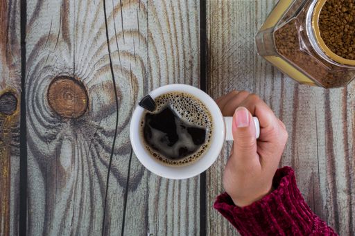 A top view of woman hands holding a cup of coffee on a wooden table