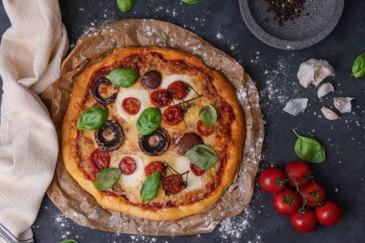A top view of whole vegetarian pizza with mushrooms, basil, tomatoes, and cheese