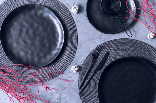 A top view of a black plate, fork, knife, strainer, and placemat with red dried twigs on the table