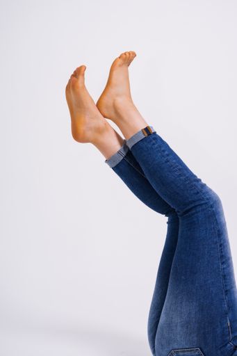A vertical shot  of a female wearing jeans with her legs lifted upward isolated on white background