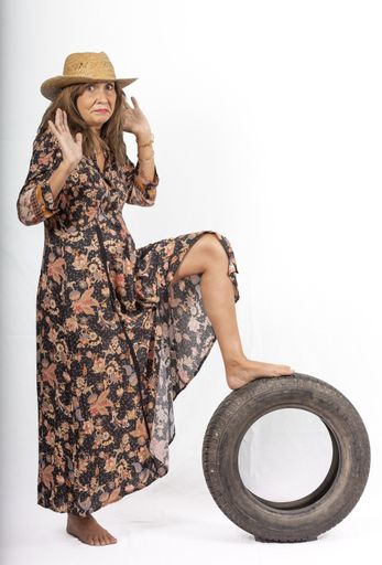 A vertical closeup of a beautiful middle-aged Hispanic woman in a straw hat posing at the camera with a tire on a white background