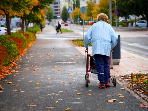 A closeup shot of a senior lady walking on the street with a walker