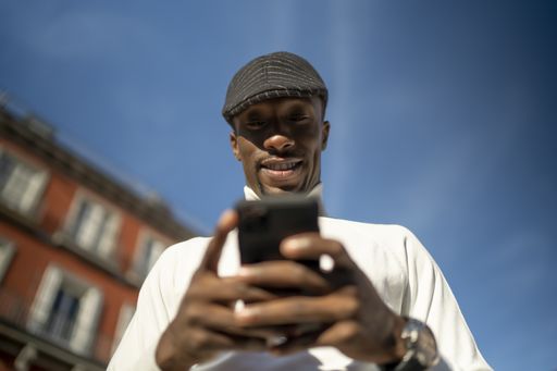 A closeup shot of a black man wearing a turtleneck and a hat looking at his phone