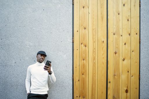 A closeup shot of a black man wearing a hat and a turtleneck looking at his phone