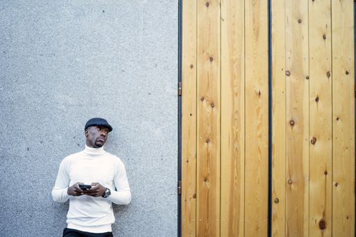 A closeup shot of a black man wearing a hat and a turtleneck holding his phone