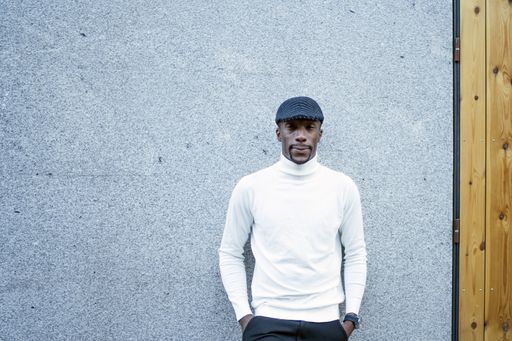 A closeup shot of a black man wearing a hat and a turtleneck