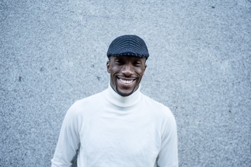 A closeup shot of a black man wearing a hat and a turtleneck