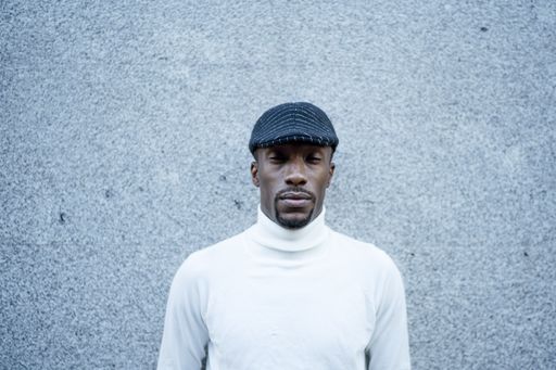 A closeup shot of a black man wearing a hat and a turtleneck