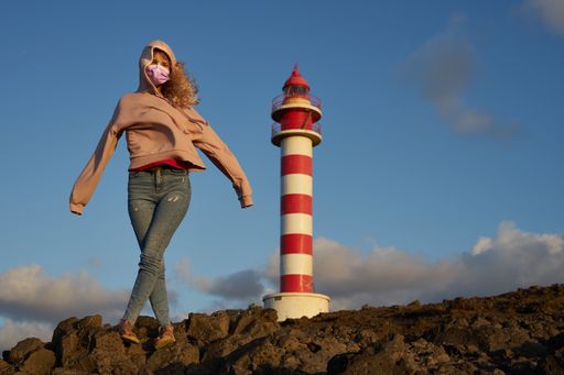 A blonde young caucasian female in a protective face mask standing in front of a lighthouse