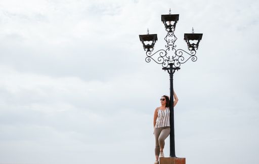 Caucasian woman leaning on a lamppost white clouds