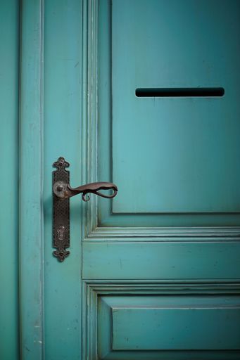 A vertical shot of a green door with an old handle and letter hole