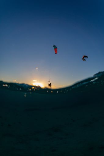 A vertical shot of people flying parachutes under the breathtaking sunset over the ocean in Kitesurfing. Bonaire, Caribbean