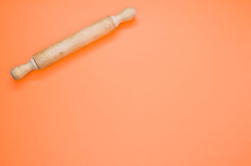 A high angle shot of a rolling pin on an orange surface