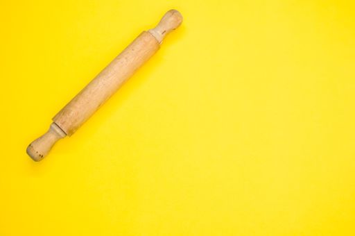 A high angle shot of a rolling pin on a yellow surface