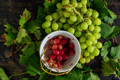 A top view of the red grapes  in the bowl next to the green grapes on the wooden surface