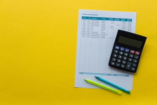 A closeup shot of a calculator, document with income and expenses, and pens on vibrant yellow background