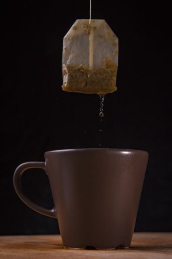 A vertical shot of a brown mug with hanging dripping tea bag against black background