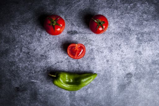 An overhead shot of three tomatoes and a pepper forming a face on concrete surface