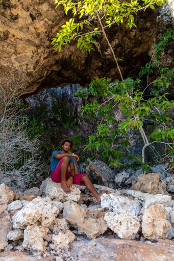A vertical shot of a male sitting on rocks looking at the camera in Bonaire, Caribbean