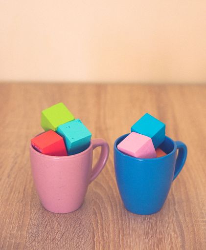 A vertical closeup shot of two coffee cups filled with toy blocks on a wooden table