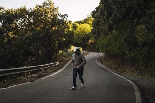 A closeup shot of a young man running in the middle of a street wearing a helmet