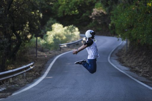 A male wearing a helmet while jumping in the middle of a road