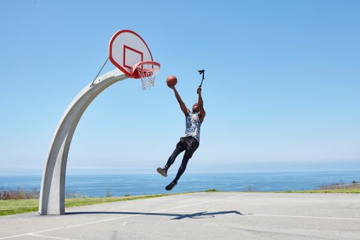 A young African-American sportsman making a dunk and recording the process with a selfie stick
