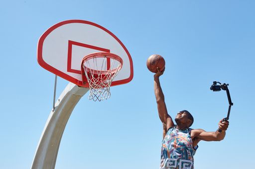 Social influencer jumping with a basketball for a selfie-stick camera on a beautiful sunny day. This cool basketball court overlooks the ocean.
