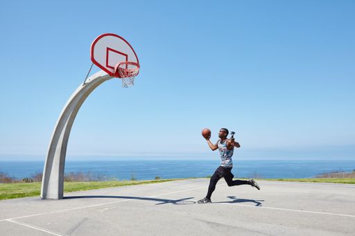 Social influencer running with a basketball for a selfie-stick camera on a beautiful sunny day. This cool basketball court overlooks the ocean.